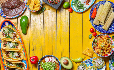 Mexican festive food for independence day independencia - chiles en nogada, tacos al pastor, chalupas pozole, tamales, chicken with mole poblano sauce. Yellow background.