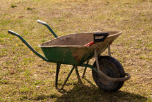 There Is An Old Garden Wheelbarrow With A Shovel In The Field