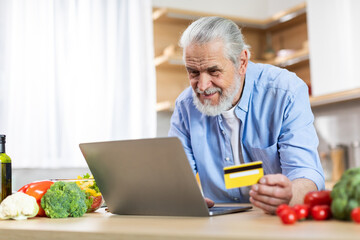 Senior Man Using Laptop And Credit Card In Kitchen, Ordering Groceries Online