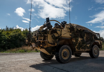 detailed close-up of a British army Supacat Jackal 4x4 rapid assault, fire support and reconnaissance vehicle in action on a military exercise, blue sky with scattered white cloud