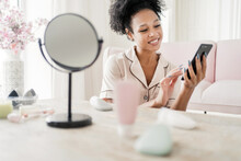 Relaxing With A Phone At Home Uses A New Face Cream. A Woman Is Engaged In Skin Care With The Help Of Cosmetics.
