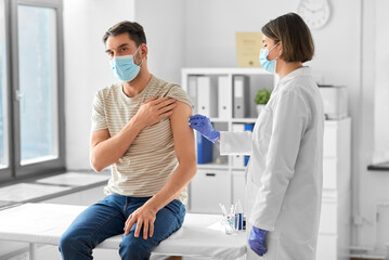 Sticker - health, medicine and pandemic concept - female doctor or nurse in protective medical mask and gloves disinfecting male patient's skin at hospital