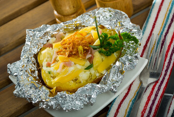 Image of tasty cooked baked in foil potatoes with bacon, cheese and fried onion