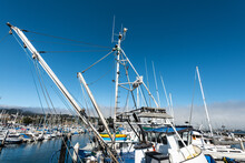 Details From Masts And Equipment Of Fishing Boat Docked In Marina With Many Sailboats Under Blue Sky With Coastal Cloud Bank