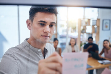 Business man writing on sticky note in meeting, doing creative advertising presentation on glass board in workshop and training employees in work office. Corporate worker planning on post it paper