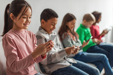 Wall Mural - Diverse Children Using Phones Playing Mobile Games Over Gray Background