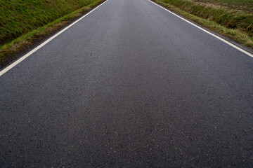 Close up of an asphalt road between grassy fields in autumn