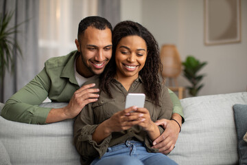 Wall Mural - Happy Black Spouses Using Cellphone Texting At Home