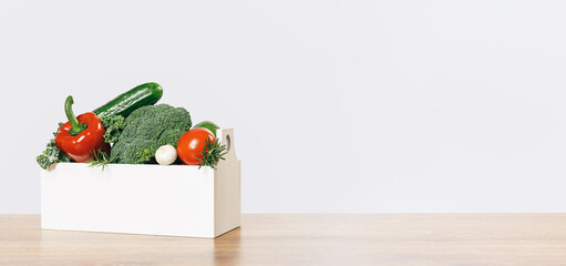 Wall Mural - Fresh green and red vegetables in a box on a wooden table. Banner with copy space. Green vegetarian diet or cuisine. Grocery delivery or shopping online. Green diet