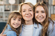 © sofiko14 - Portrait of happy mother hugging two little kids. Joyful affectionate mom cuddling sweet sibling daughters, looking at camera with toothy smile. Family relationship, motherhood. Head shot.