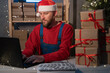Small business aspiring entrepreneur, SME freelance worker working in a home office man in Santa Claus hat and accepts an online order using an application and a laptop, Christmas sale