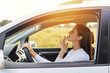 © sementsova321 - Side view portrait of dark haired beautiful woman driving a car and looking at mirror touching up her makeup, attractive female traveling alone on sunset.