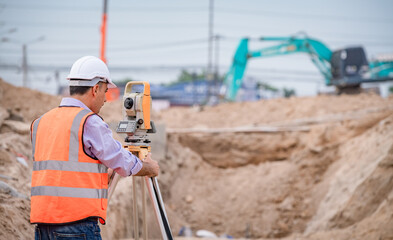 Wall Mural - Surveyor engineer wearing safety uniform ,helmet and radio communication with equipment theodolite to measurement positioning on the construction site of the road with construct machinery background