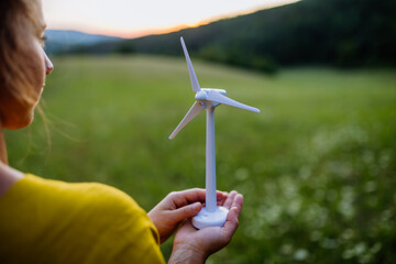 Close up of hands holding model of wind turibe in nature. Concept of ecology future and renewable resources.