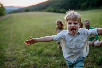 Wall Mural - Happy young family spending time together outside in green meadow, little boy running and enjoying nature.