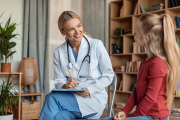 Friendly female doctor pediatrician talking to little girl patient at checkup consultation, pediatrist consulting kid