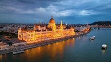 Illuminated Hungarian Parliament Building With The Danube River, After Sunset In Budapest, Hungary. 4K Aerial Drone View