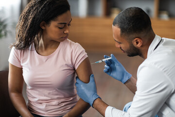 Handsome black man making injection in shoulder for female patient