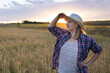 © olga_sova - A beautiful middle-aged farmer woman in a straw hat and a plaid shirt stands in a field of golden ripening wheat during the daytime in the sunlight