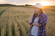 © olga_sova - A beautiful middle-aged farmer woman in a straw hat and a plaid shirt stands in a field of golden ripening wheat during the daytime in the sunlight