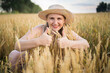 © olga_sova - A beautiful middle-aged farmer woman in a straw hat and a plaid shirt stands in a field of golden ripening wheat during the daytime in the sunlight