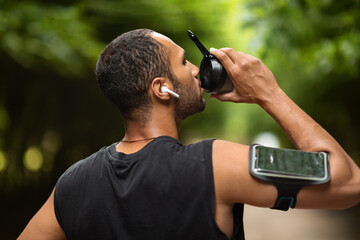 Wall Mural - Athletic african american man drinking water, exercising at park