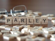 Parley Word Or Concept Represented By Wooden Letter Tiles On A Wooden Table With Glasses And A Book