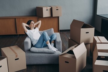 Wall Mural - Female sitting on armchair relaxes during packing boxes on moving day to new home. Easy relocation