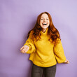 © contrastwerkstatt - laughing redhead woman with yellow sweater, copyspace with purple background