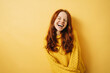 Laughing redhead woman with closed eyes and yellow sweater, copyspace against yellow background