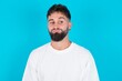 © Jihan - bearded caucasian man wearing white T-shirt over blue background, looks pensively aside, plans actions after university, imagines what to do Thinks over about new project.