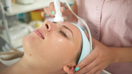 beautician therapist applying face treatment in beauty salon to young woman.