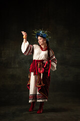 Wall Mural - Art portrait of beautiful woman wearing traditional folk Ukrainian costume posing isolated over dark vintage background. Fashion, beauty, cultural heritage