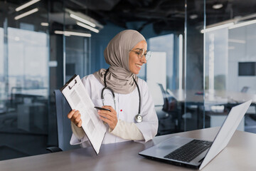 Doctor online consultation with patient, muslim woman in hijab working remotely with laptop for video call, consulting patients sitting inside modern clinic office