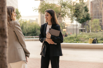 Wall Mural -  Positive young caucasian female colleagues talking during outdoor coffee break. Ladies have fun, wear jackets. Business people concept