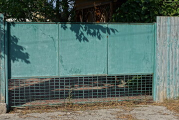 Sticker - one old big closed iron gate and part of a gray wooden fence on a rural street 