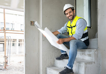 Engineer man reading blueprint as sitting at home improvement construction site. Professional architect wears safety hardhat is working on home interior, housing development project. Copy space.