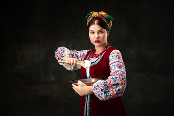 Wall Mural - Creative portrait of beautiful Ukrainian woman wearing traditional folk costume isolated over dark vintage background. Traditions, history, fashion, beauty,