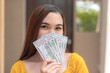 Young Asian woman wearing a yellow top holds a 500 dollar bill in her hand. Covering mouth with dollar bills.