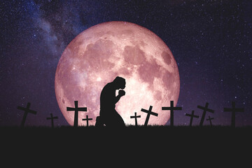 Wall Mural - The idea of ​​praying for peace to reduce the loss of war. A Christian man prays in a field with graves and moons.