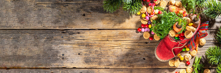 Sinterklaas, Saint Nicholas day background. Little kid red shoe with carrots and sweets, trooigoed, pepernoten, candy. Dutch Christmas holiday on cozy wooden background.