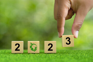 Wall Mural - 2023. enviromental sustainability target. Hand puts wooden cubes with number 3 icons with 2023 icons on green background. green community. Goals,plan,opportunity, new green business and social.