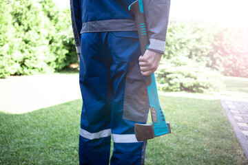 Close up of handyman holding axe and standing on grass in backyard