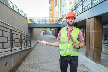 Male architect in orange helmet holding blueprint and presenting empty hand
