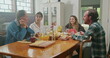 © Marco - Middle aged parents having breakfast with young daughter and oldest son. Mother serves cheese bread to her husband. The son eats bread they chat happily.