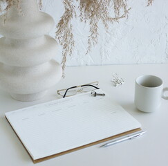 weekly planner mockup with copy space on home desk workspace with modern vase, pen, cup coffee top view on white table.  Minimalist lifestyle neutral colors.