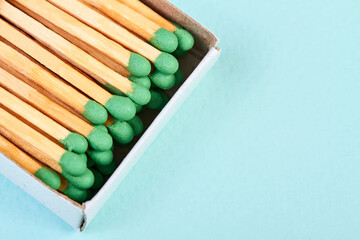 Many matches with green heads in a matchbox on a blue background with copy space