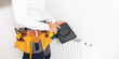 Man in work overalls using wrench while installing heating radiator in room. Young plumber installing heating system in apartment. Concept of radiator installation, plumbing works and home renovation.
