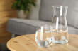 Jug and glass of water on wooden table in room, space for text. Refreshing drink