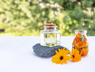 Two bottles of essential oil and calendula flowers for the care of women's skin on a natural background. Stone podium. Front view